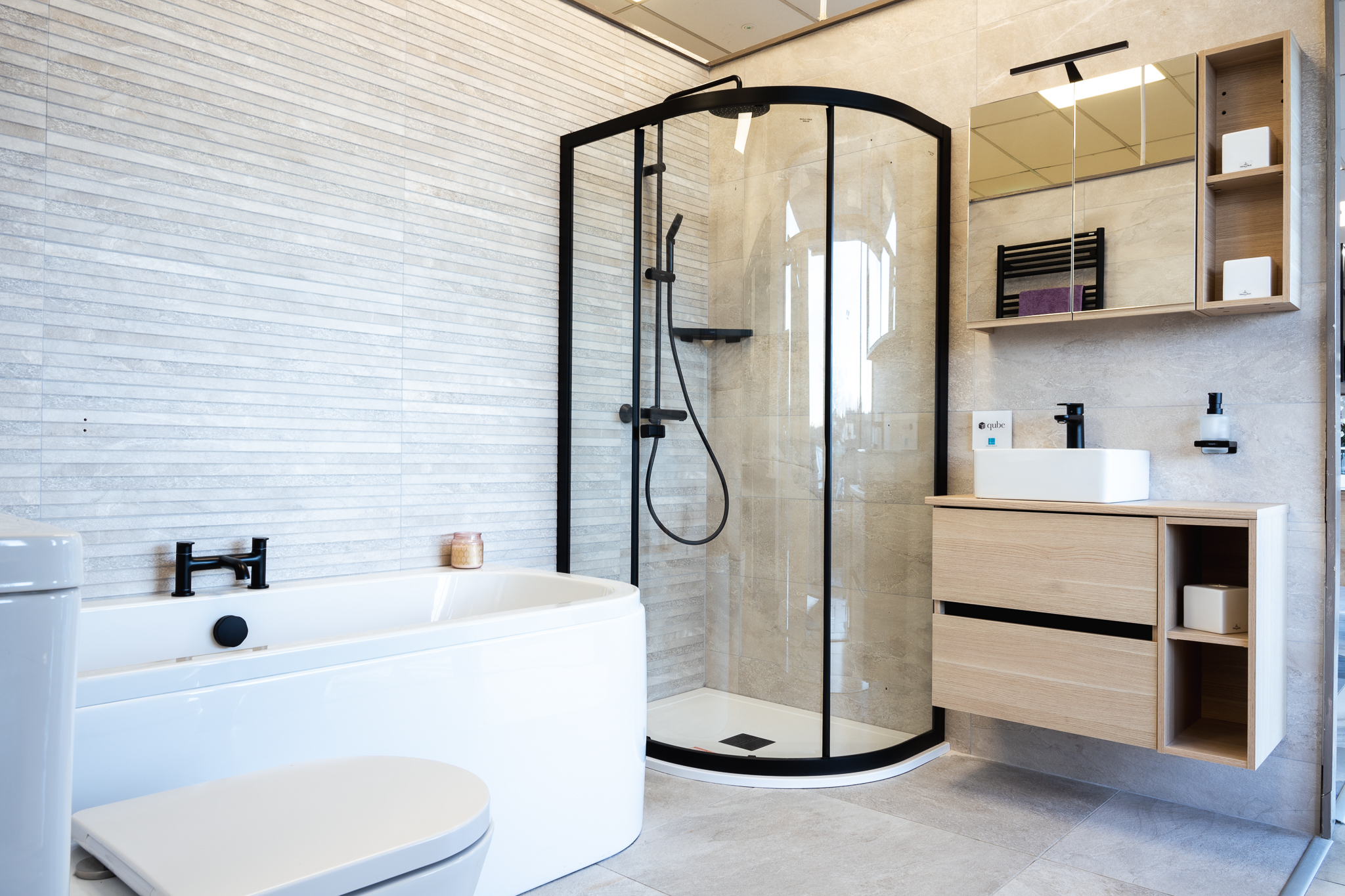 A showroom bathroom with a black-framed quadrant shower, an oak vanity with open shelving and stone-effect wall tiles