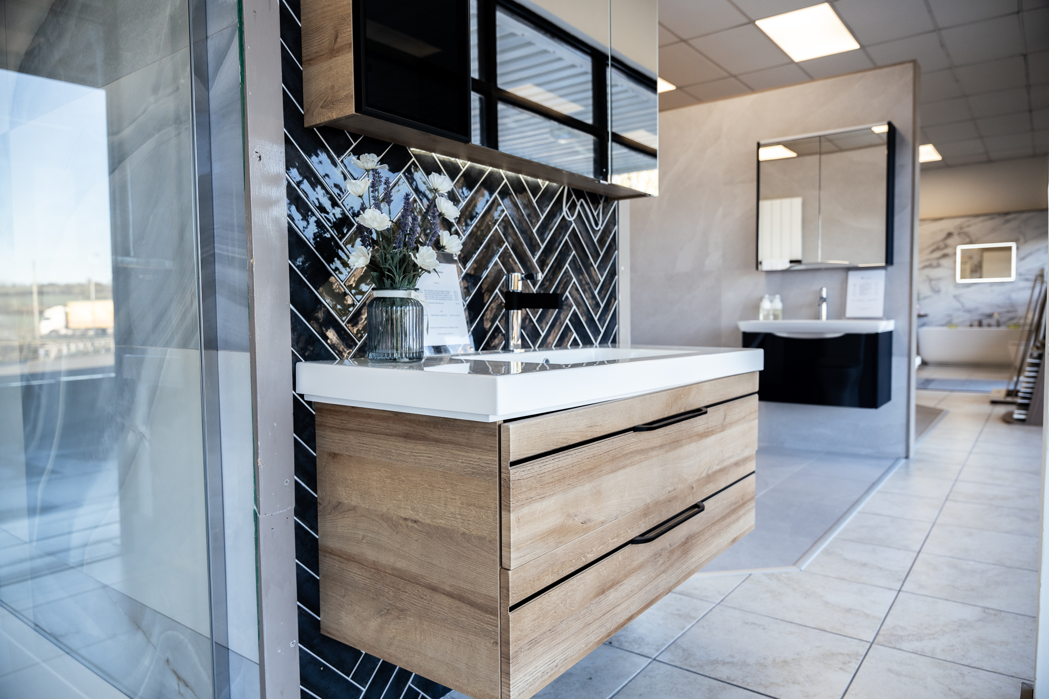 An oak-effect vanity unit with a white basin and black tap, set against navy herringbone wall tiles