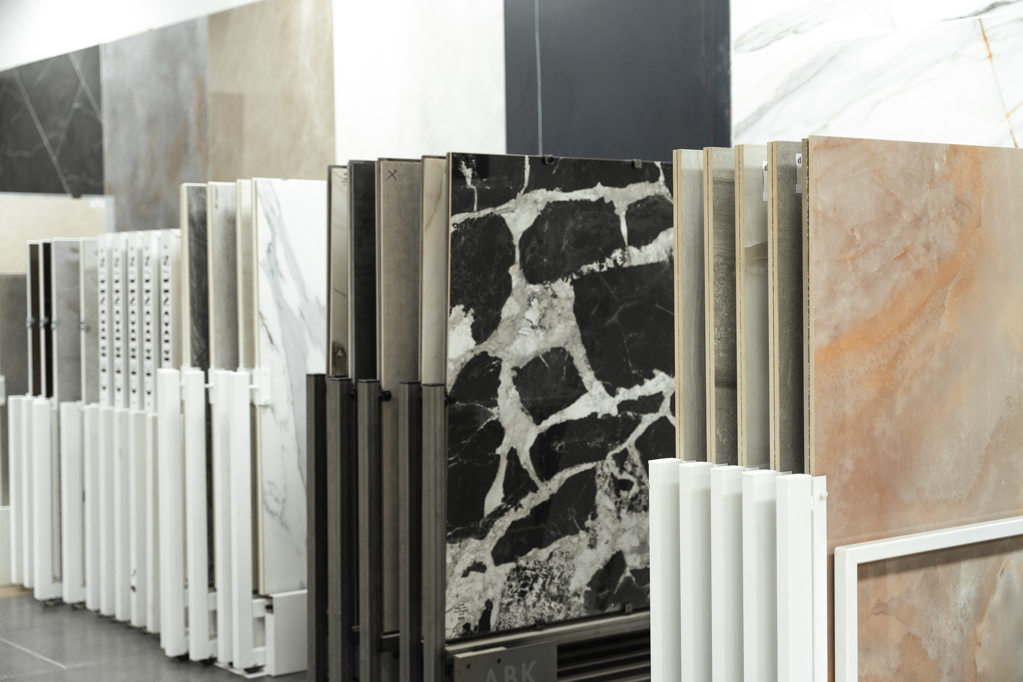 Large tile slabs on showroom display racks, including a black and white marble effect and a warm onyx-look finish